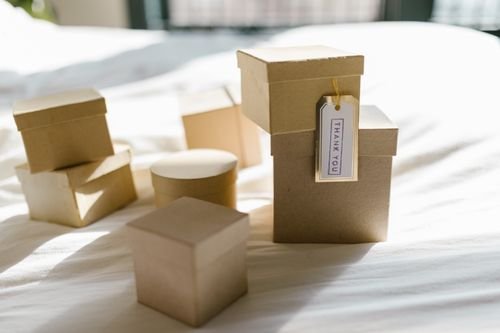 Plusieurs colis en carton de tailles variées posés sur un lit servent à illustrer l’expédition d’objets personnalisés.